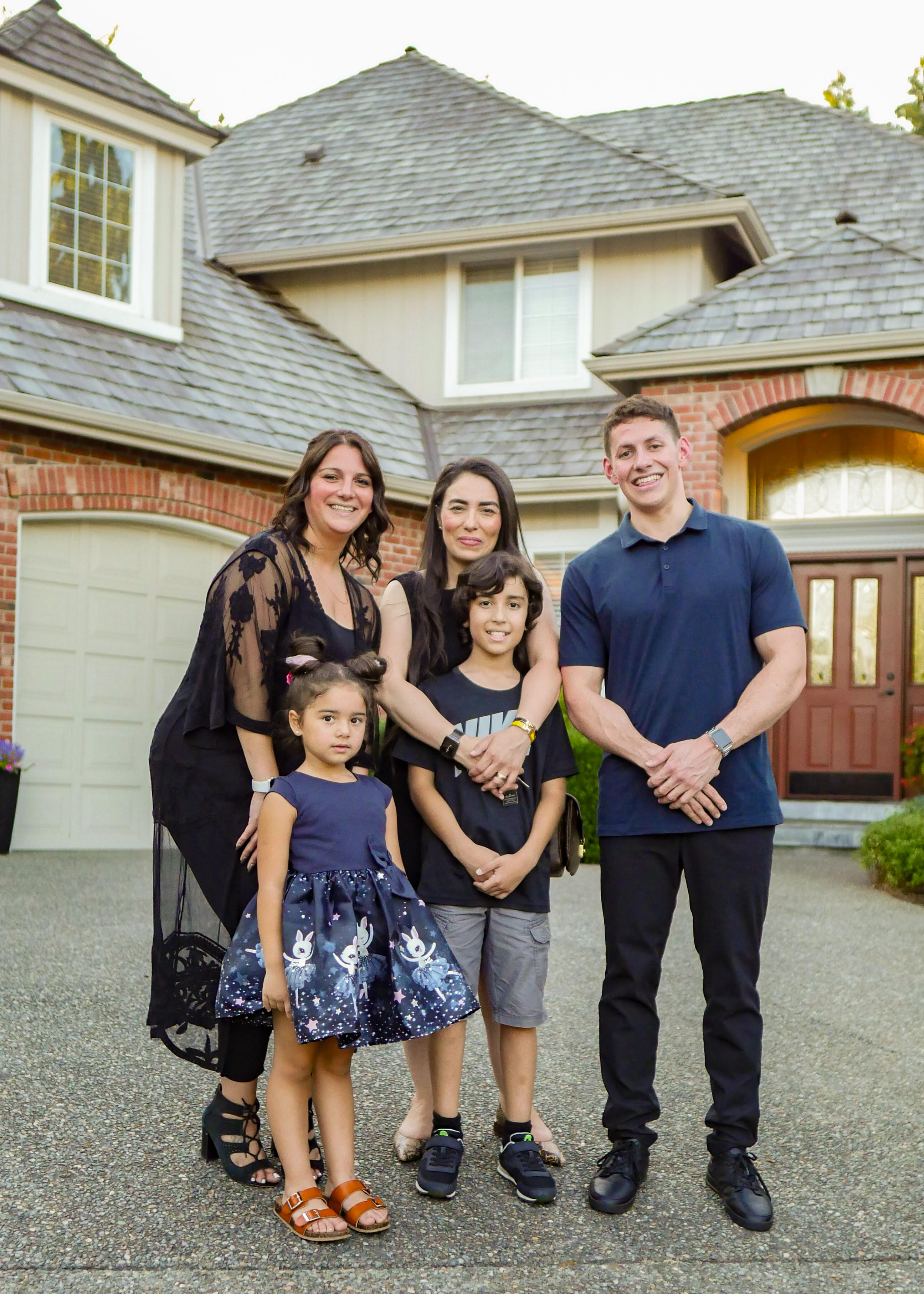 Blake Brown in a navy polo, smiling with his family in front of a brick home